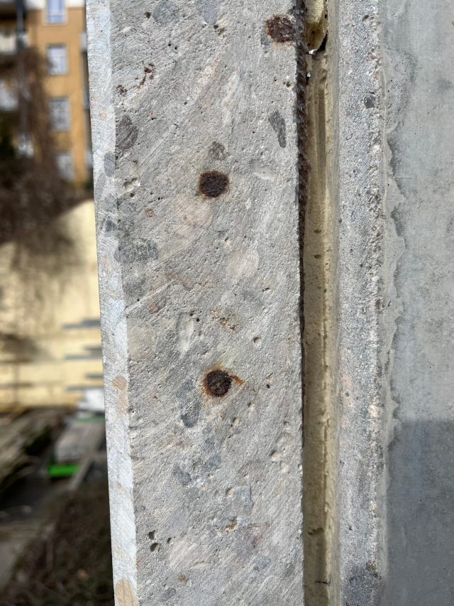 Nahaufnahme einer Betonwand mit sichtbaren Rostflecken und Rissen, die auf eine Instandsetzung hindeuten.