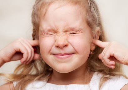 Child with autism plugging her hears and shutting her eyes tight. 