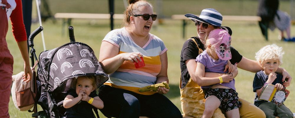 Two people with babies chatting and laughing in the audience at SO Festival