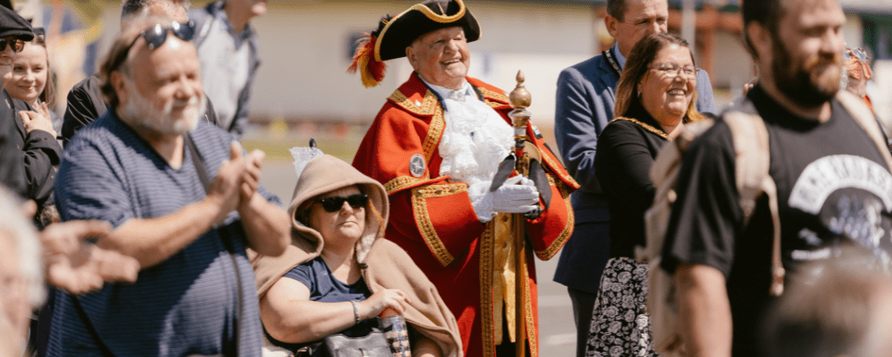 The Mayor of Mablethorpe and Town Cryer smiling watching a performance, surrounded by the audience.