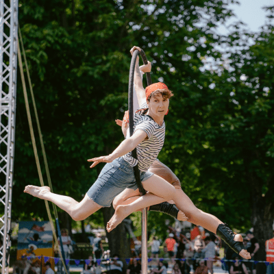 Creative heights Aerial circus performer in striped shirt doing acrobatic routine on rope at outdoor festival with crowd