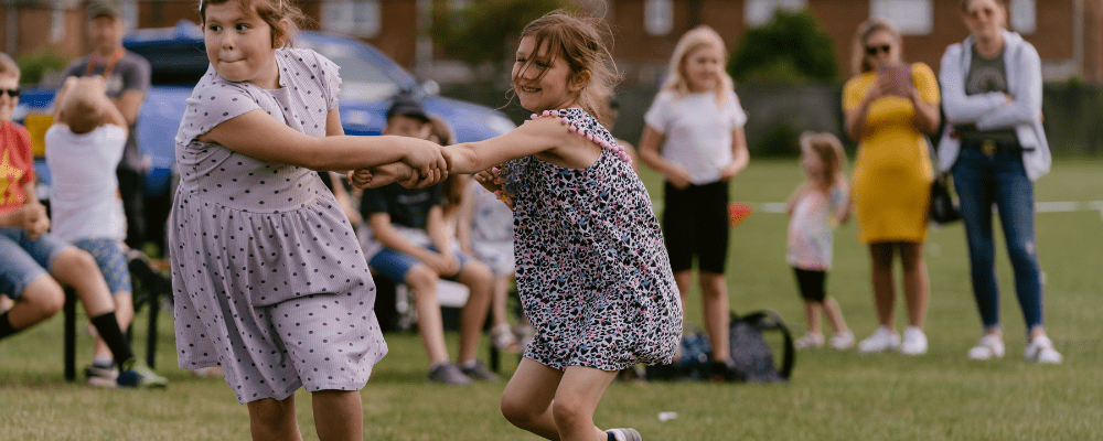 Two children playing, holding each others hands, one pulls the other as they run