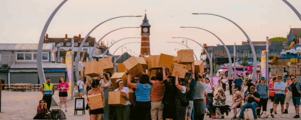 Town center community boxed activity with volunteers carrying boxes near landmark clock tower with public gathering