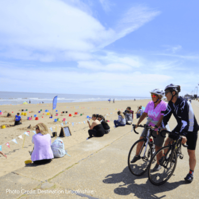 Two cyclists on a path near a busy beach