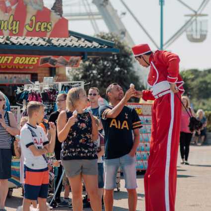 A performer on stilts handing an ice cream to an audience member