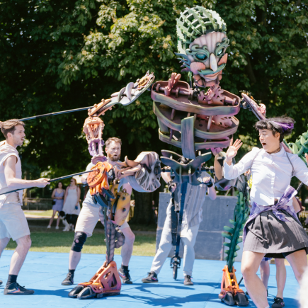 A large puppet operated by a group of performers chasing a dancer