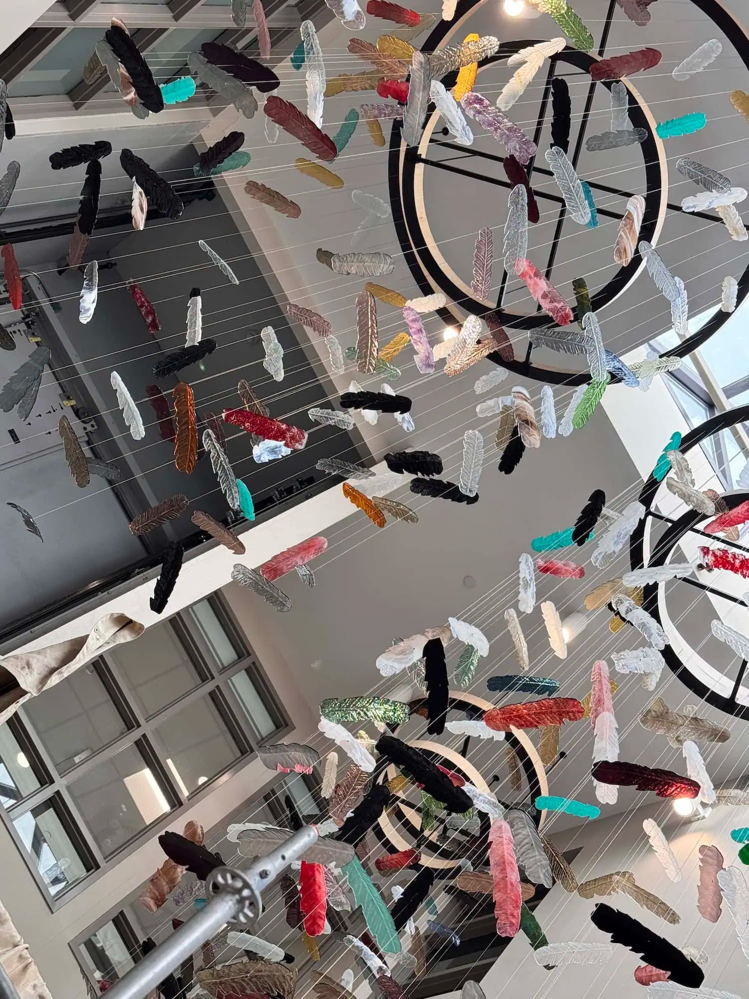 Full atrium view of Chromatic Canopy installation from mezzanine level showing scale of suspended glass feathers across multiple floors, SOAHAC London Ontario