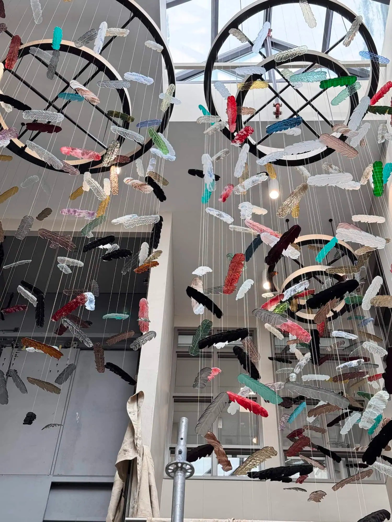 Top-down view of cedar-clad ring canopies with multicolour hand-blown glass feathers suspended in atrium, SOAHAC London Ontario 2025