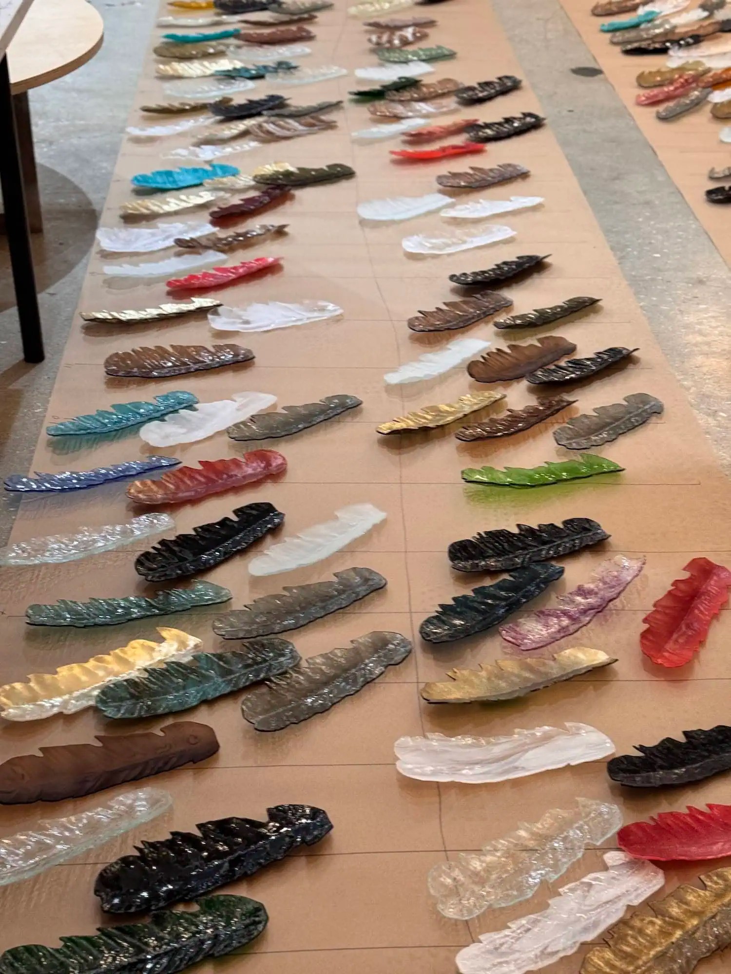 Studio floor covered with hundreds of hand-blown glass feathers in multiple colours laid out prior to installation, Soffi Studio Windsor