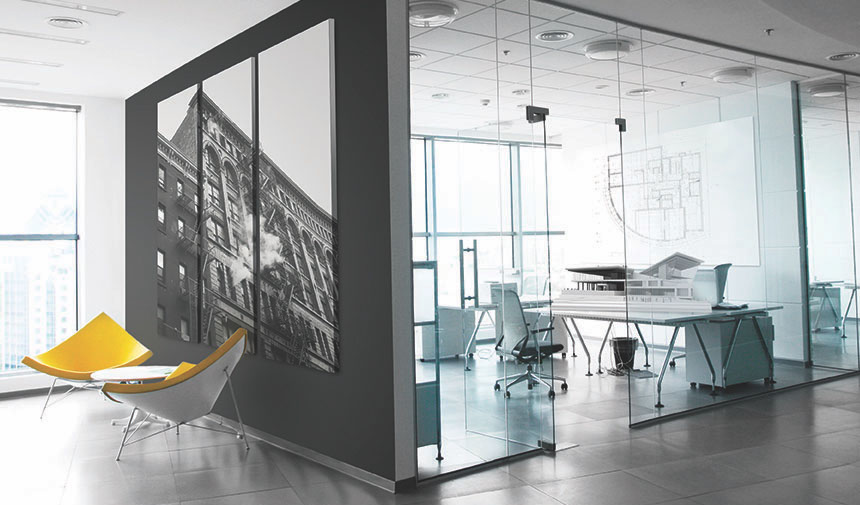 Modern office interior with glass walls, yellow chairs, and architectural blueprints.