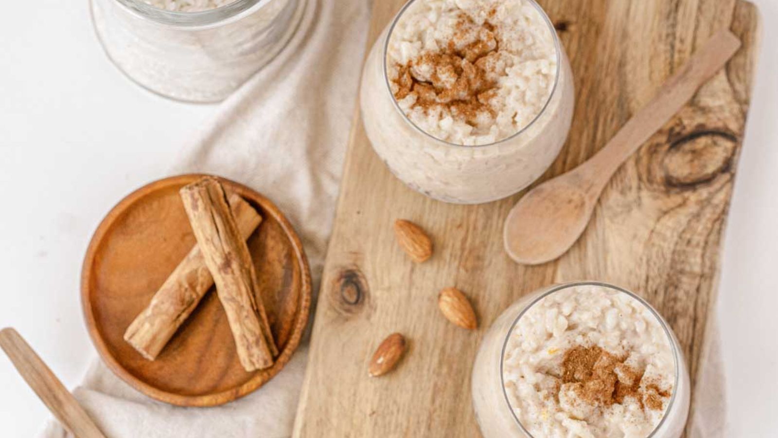 A bowl of rice pudding with cinnamon and nuts on a wooden cutting board.