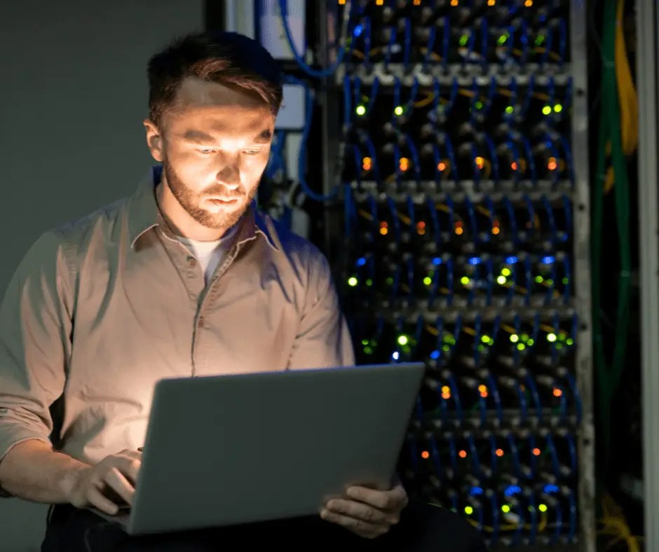 Concentrated young bearded server manager in shirt working in dark room of data center