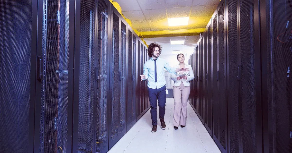 IT engineer showing working data center room to female chief engineer who is holding tablet about data center cooling