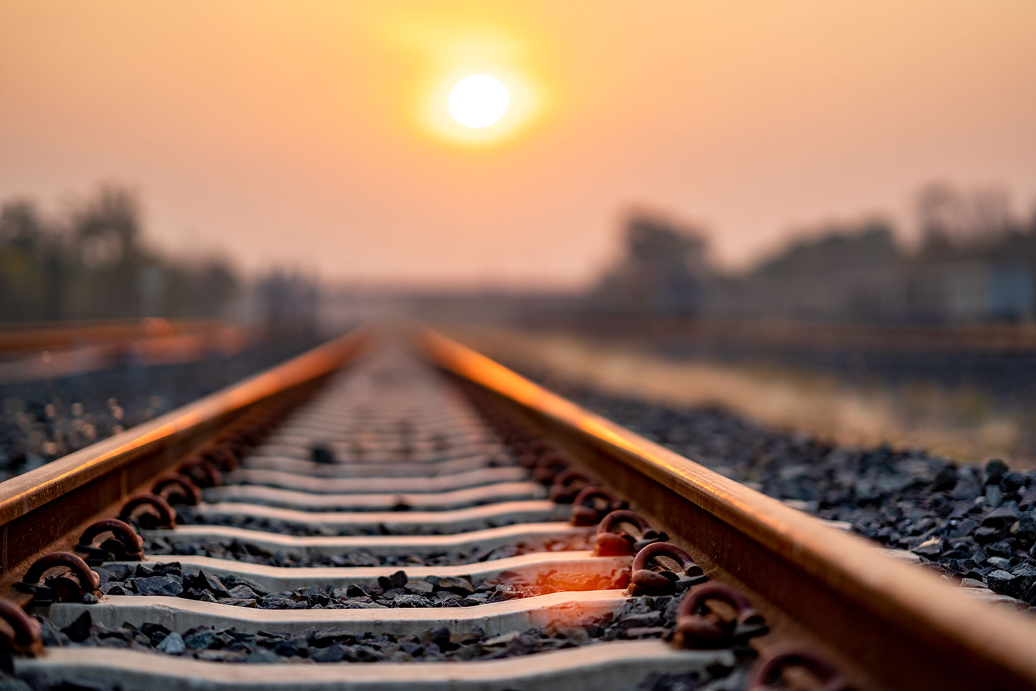 Train tracks under an orange sky with sun