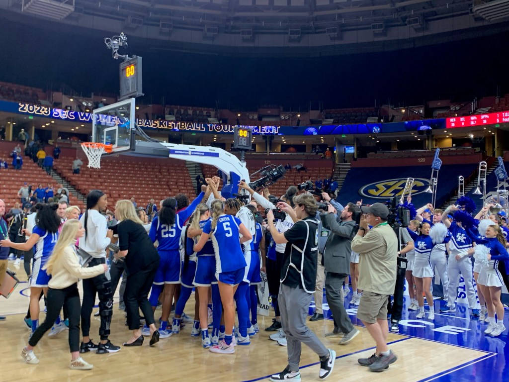 Kentucky huddles in a corner of the court, hands raised, and photographers snap photos.