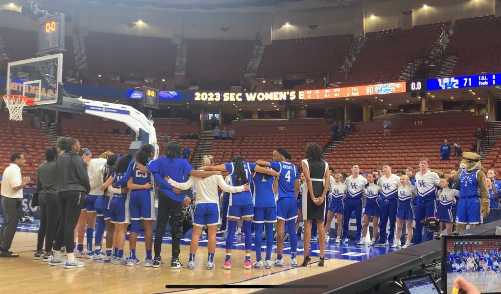 Members of the Kentucky program, along with cheerleaders and the mascot, put their arms around each other and sing.