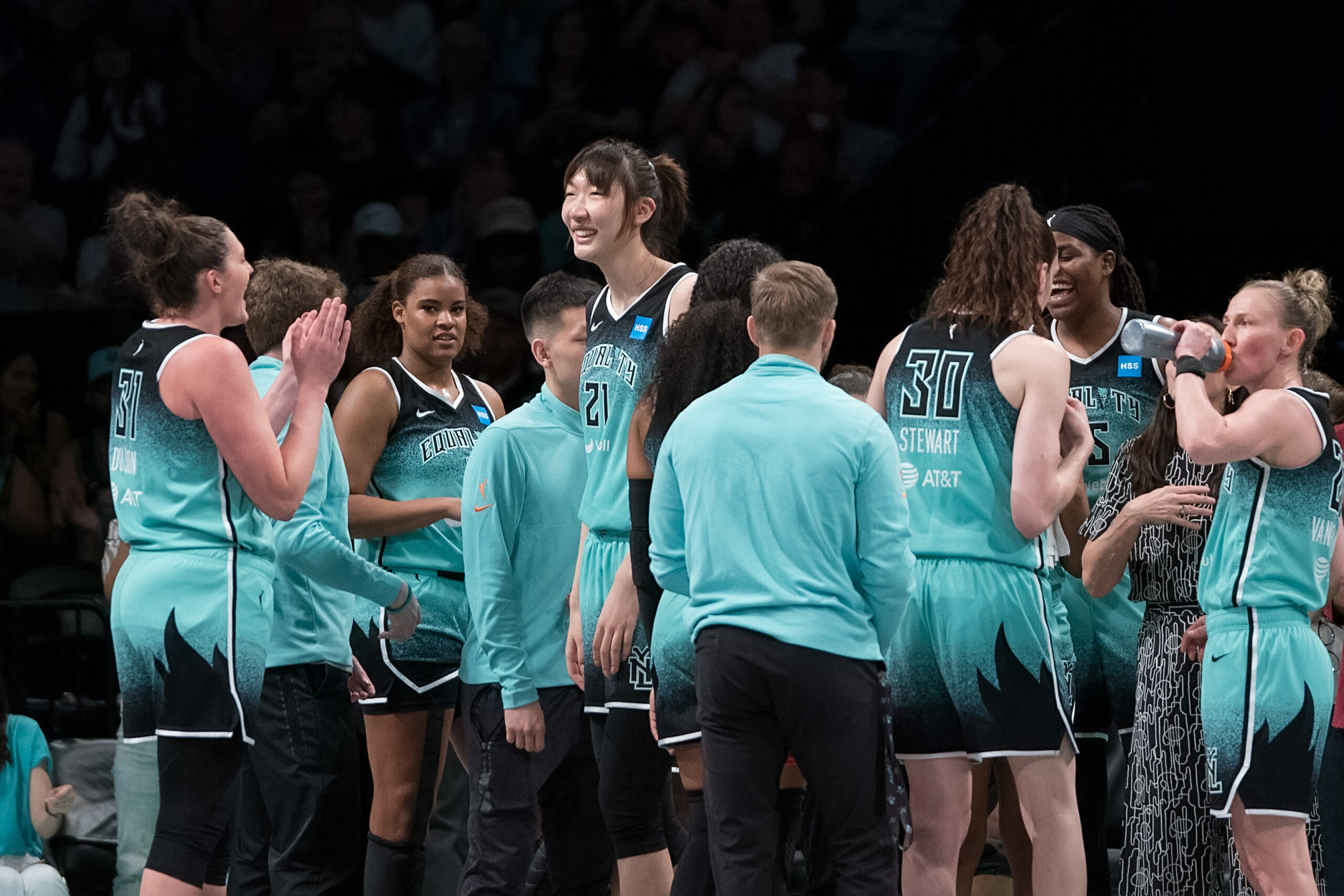 New York Liberty center Han Xu smiles as she stands in the center of a team huddle.