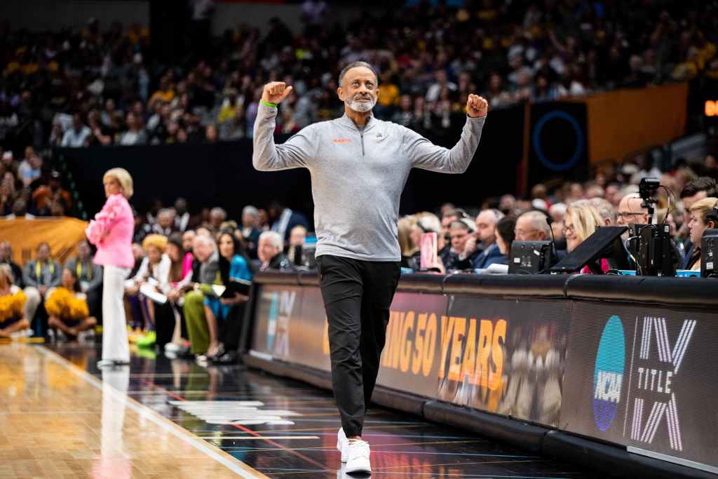 Virginia Tech head coach Kenny Brooks clenches his fists and raises both arms upward. He gazes upward and walks in the direction of his bench.