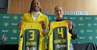 Nneka Ogwumike stands in a bright yellow blazer holding a Storm jersey emblazoned with the number three and Ogwumike's last name. She stands next to Skylar Diggins-Smith who holds a jersey with her own last name and the number four on it.