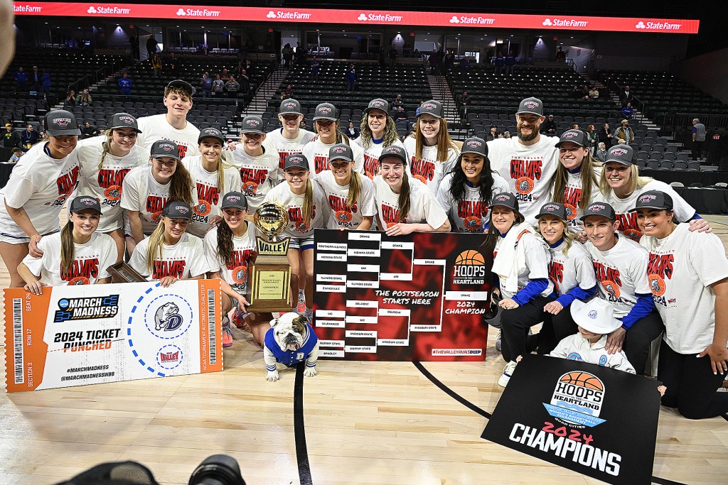 The Drake women’s basketball team poses on the court with a live dog mascot and an MVC Tournament trophy.