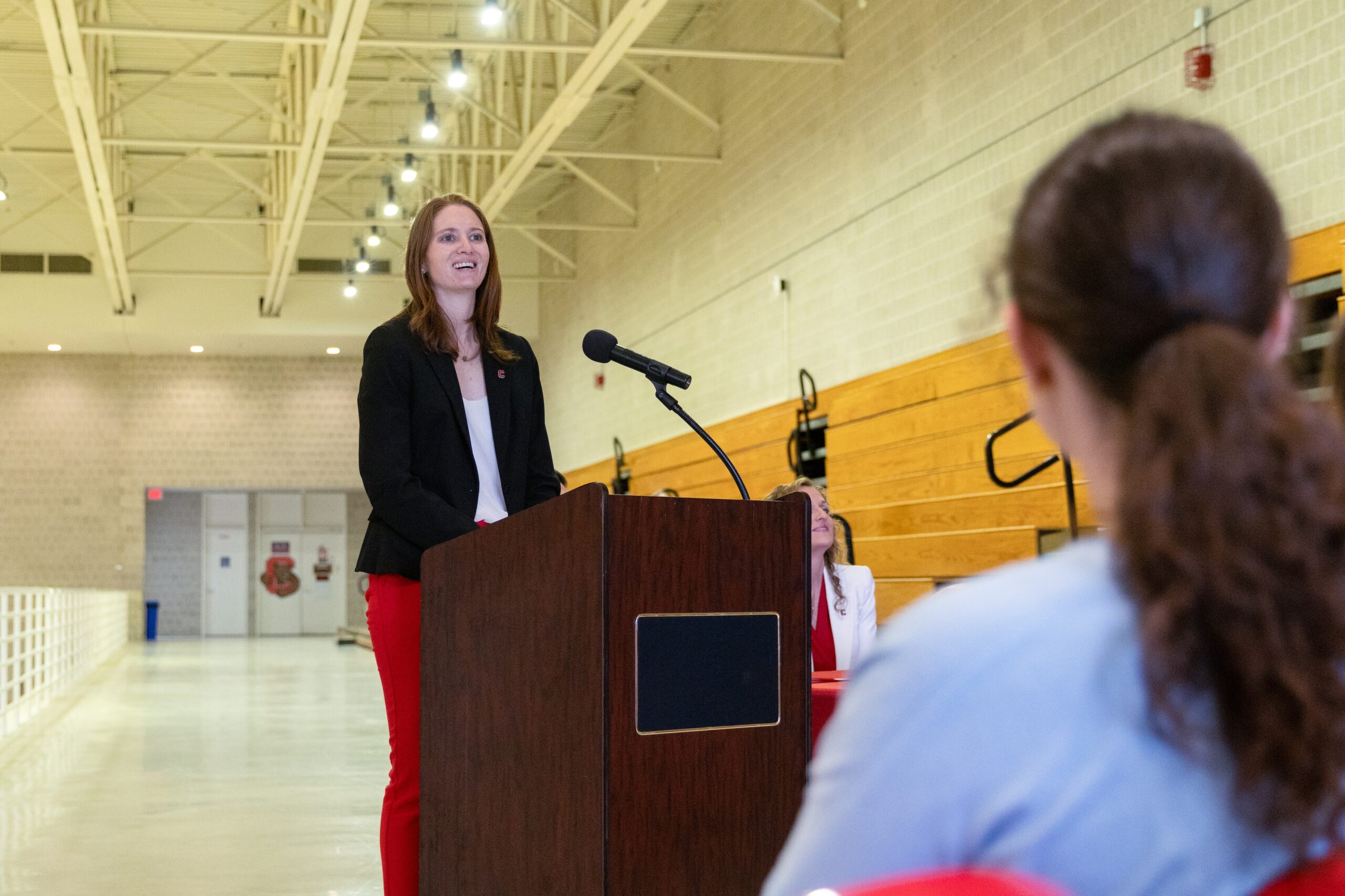 Cornell head coach Emily Garner stands at a podium and smiles as she speaks with the audience.