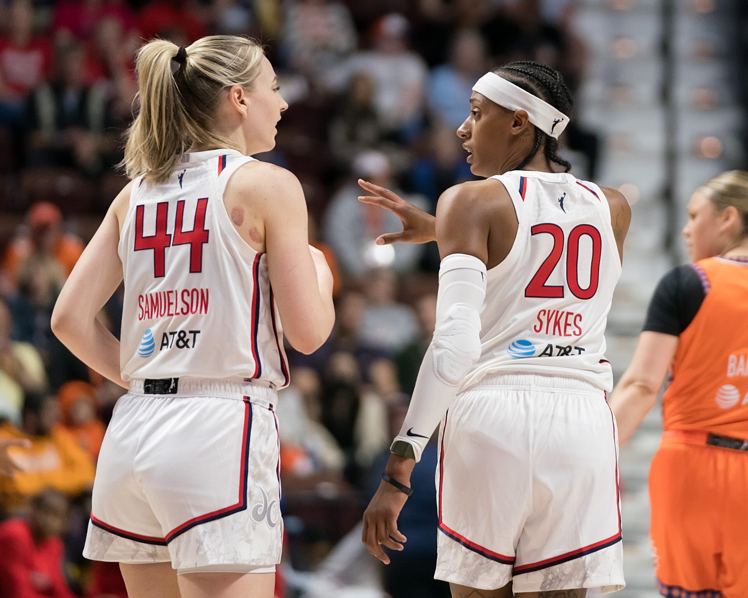 Washington Mystics point guard Brittney Sykes and wing Karlie Samuelson are photographed from behind. Sykes has a hand out in front of her as she talks.