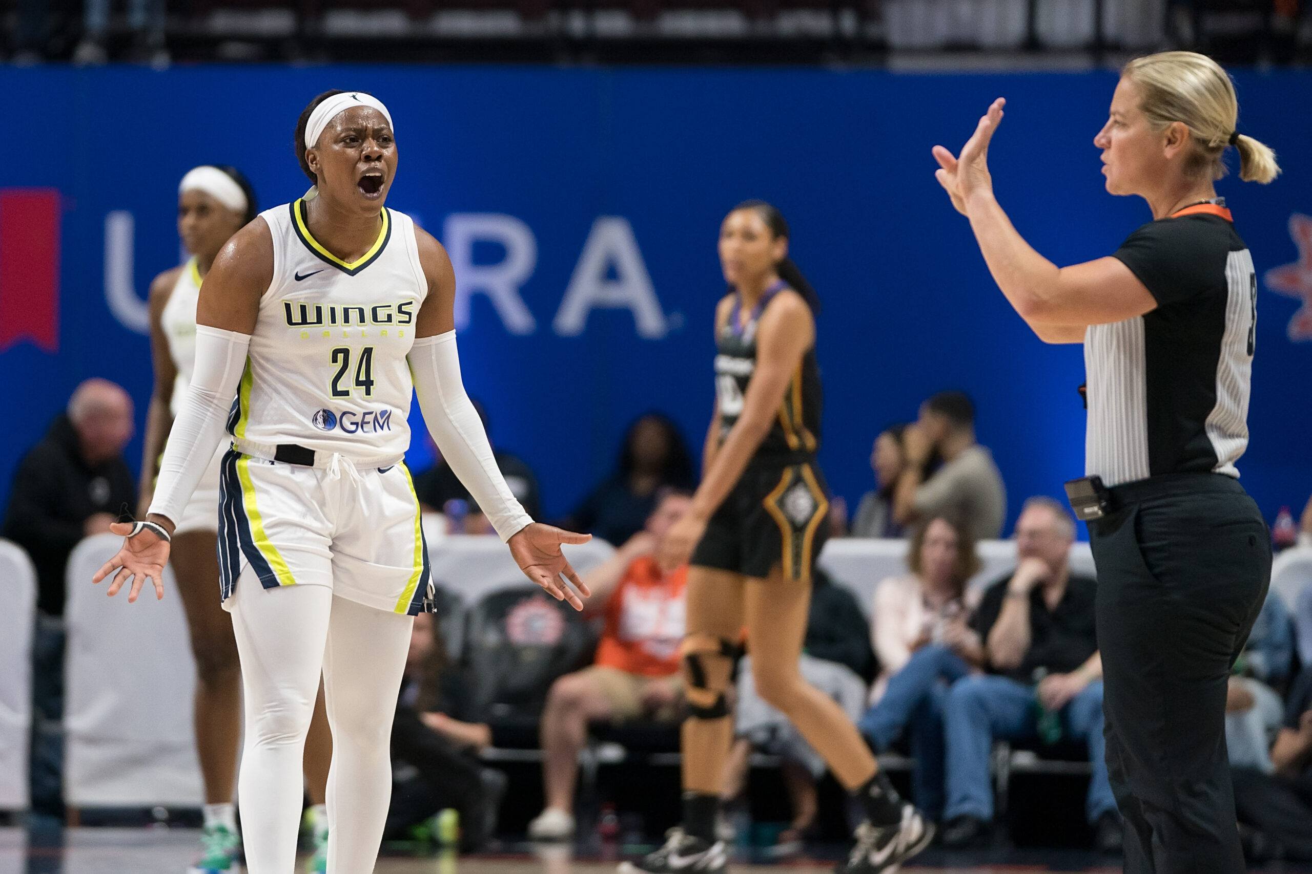 Dallas Wings guard Arike Ogunbowale (24) reacts to a call with a shocked look and her arms out as a referee has her hands up signaling the call.