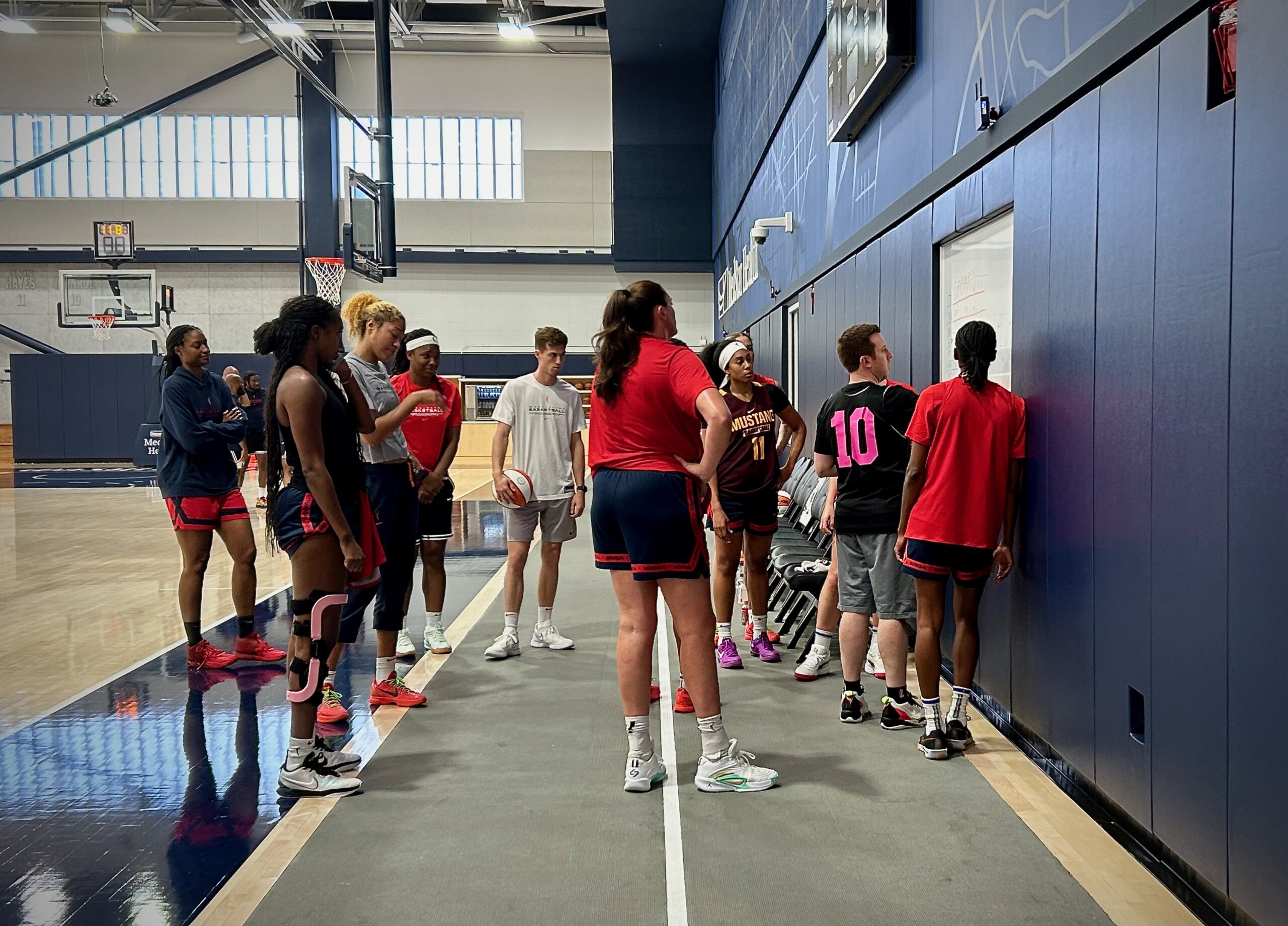Washington Mystics head coach Eric Thibault draws up a play on a permanent whiteboard at the team's practice facility as his players look on.