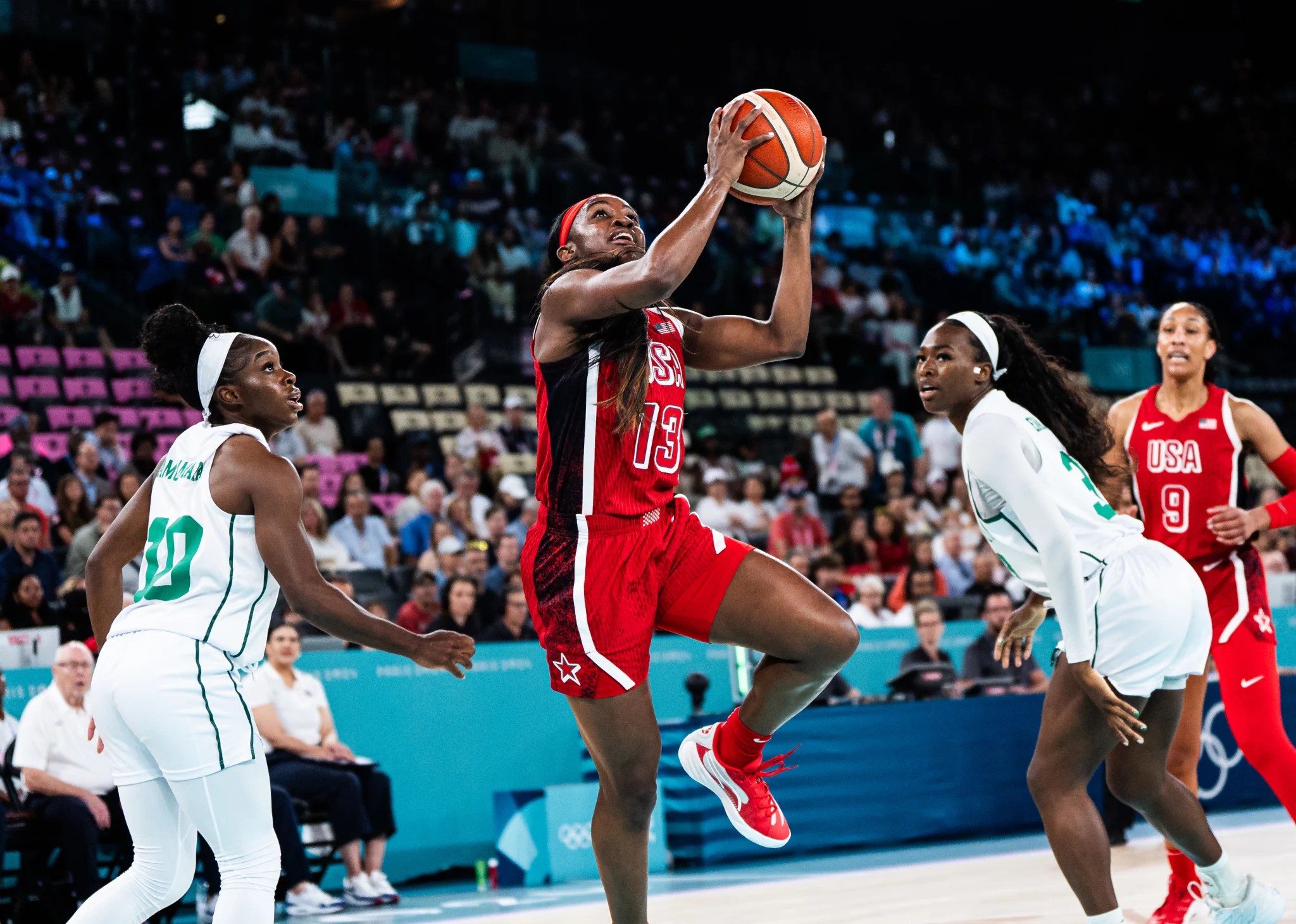 Jackie Young (13) aims for the basket while two defenders on the Nigeria team look toward her from either side. A'ja Wilson (9) looks on from behind the defenders.