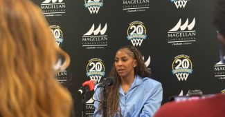 Candace Parker is sitting in front of a black, blue and white step and repeat with Chicago sky branding as she speaks into a microphone to the media.