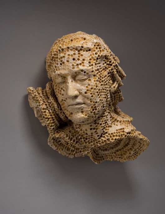 A ceramic sculpture of a sleeping figure whose face is made of honeycomb.
