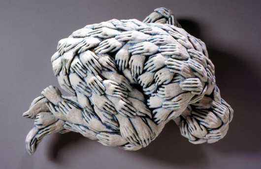 A ceramic sculpture of a curled-up figure covered in overlapping hands.