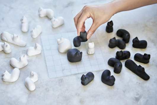 A tabletop board game with black-and-white pieces shaped like cats that can be fit onto a grid in a tight arrangement.