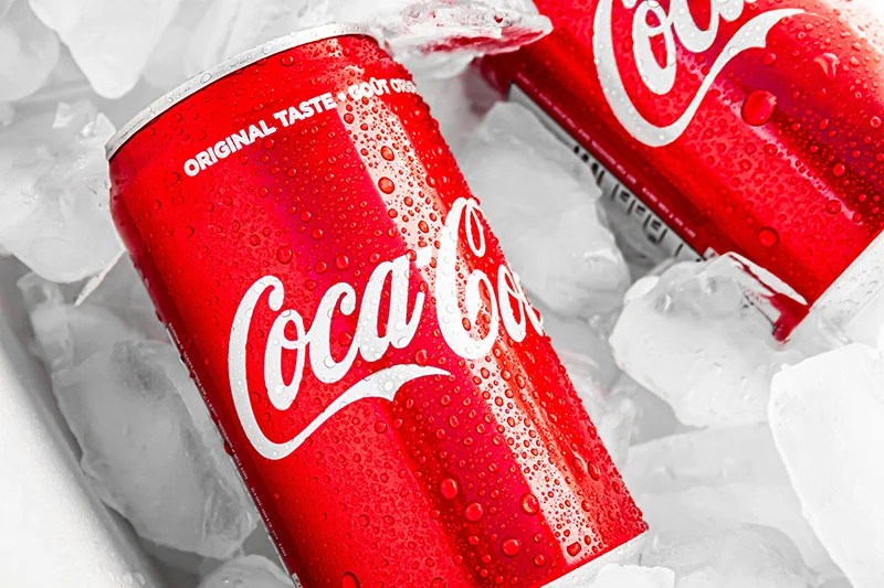 Two red Coca-Cola cans with condensation in a tub of ice cubes.