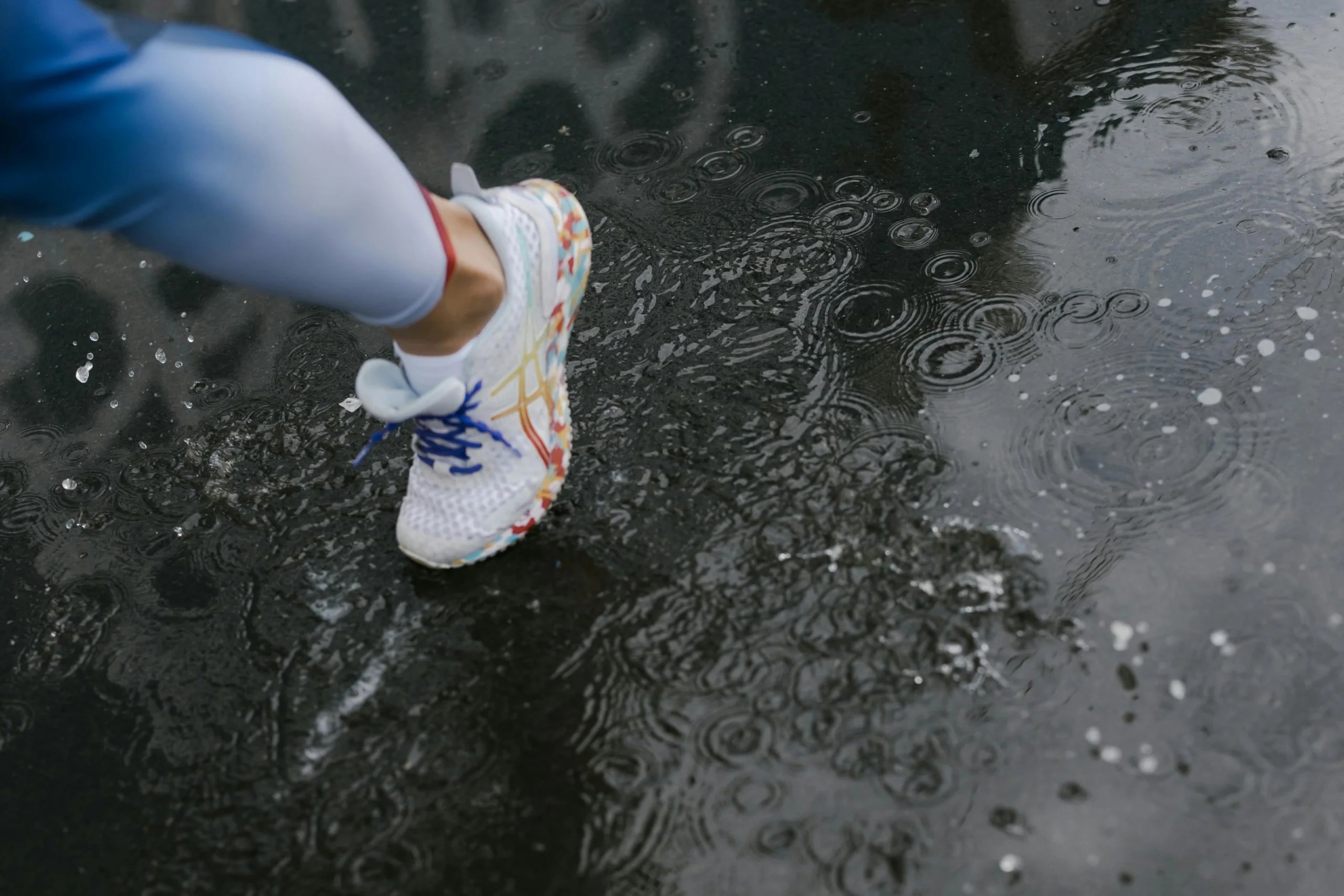 White athletic shoe with colourful accents stepping into a puddle, creating ripples and splashes.