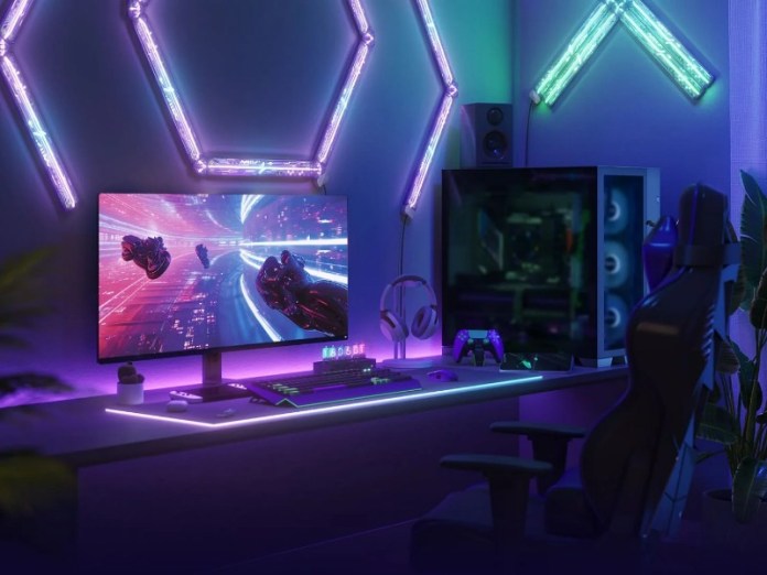 Ein dunkler „Smart Gaming Room” mit violetter, blauer und grüner Neon-LED-Beleuchtung. Auf einem Schreibtisch steht ein Gaming-PC mit Monitor, auf dem ein futuristisches Spiel zu sehen ist, eine beleuchtete Tastatur, Kopfhörer und ein violetter Controller. Violette sechseckige und grüne V-förmige LED-Lampen schmücken die Wände, daneben stehen ein Gaming-Stuhl und eine Zimmerpflanze.