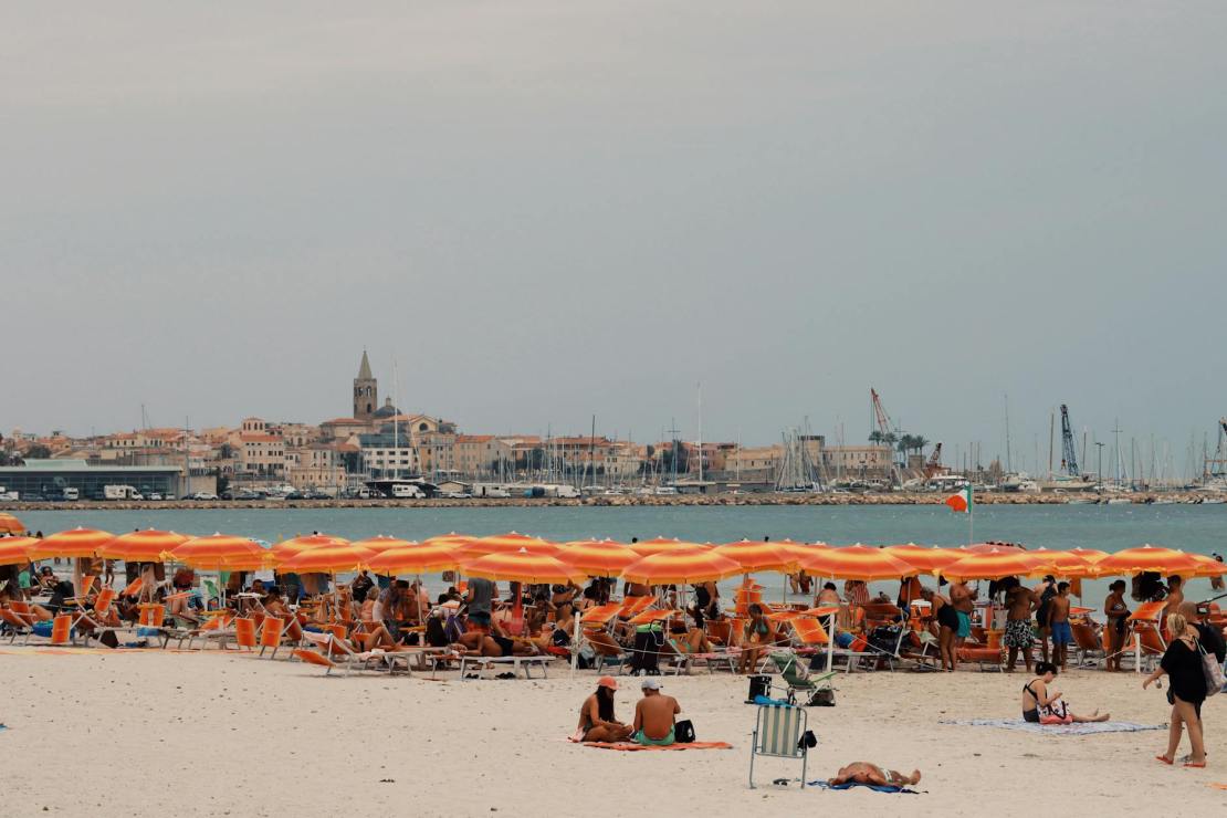 people on beach with city buildings behind sea