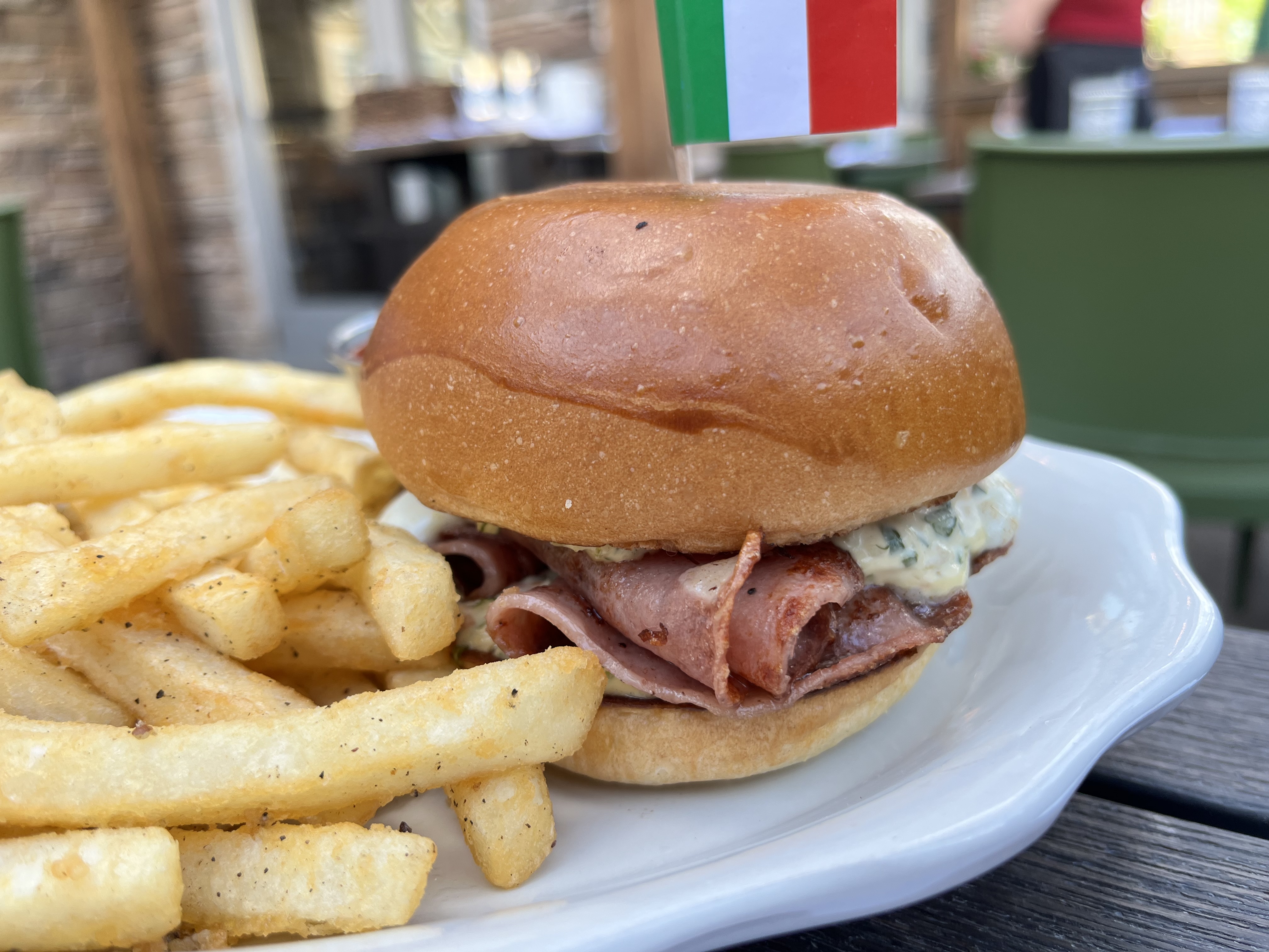 A mortadella sandwich with a little Italian flag sticking out of it on a plate with french fries