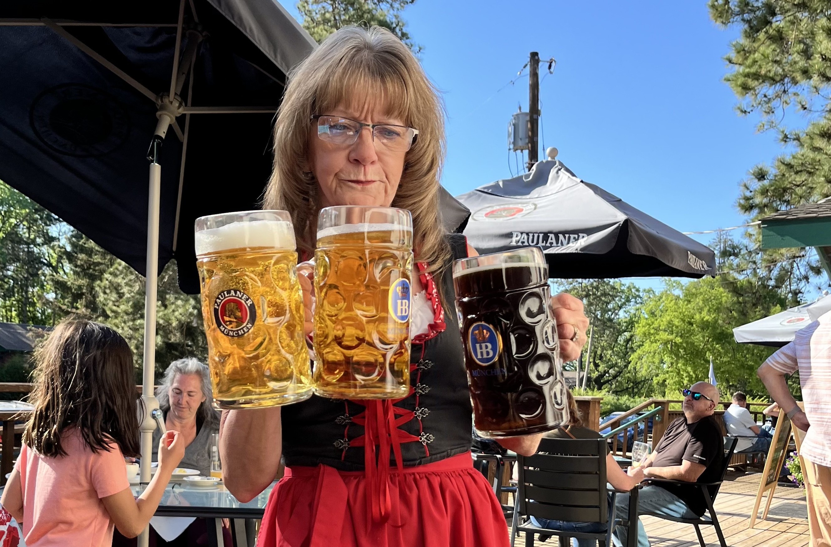 A woman in a traditional German dirndl dress carries three liters of beer in large mugs