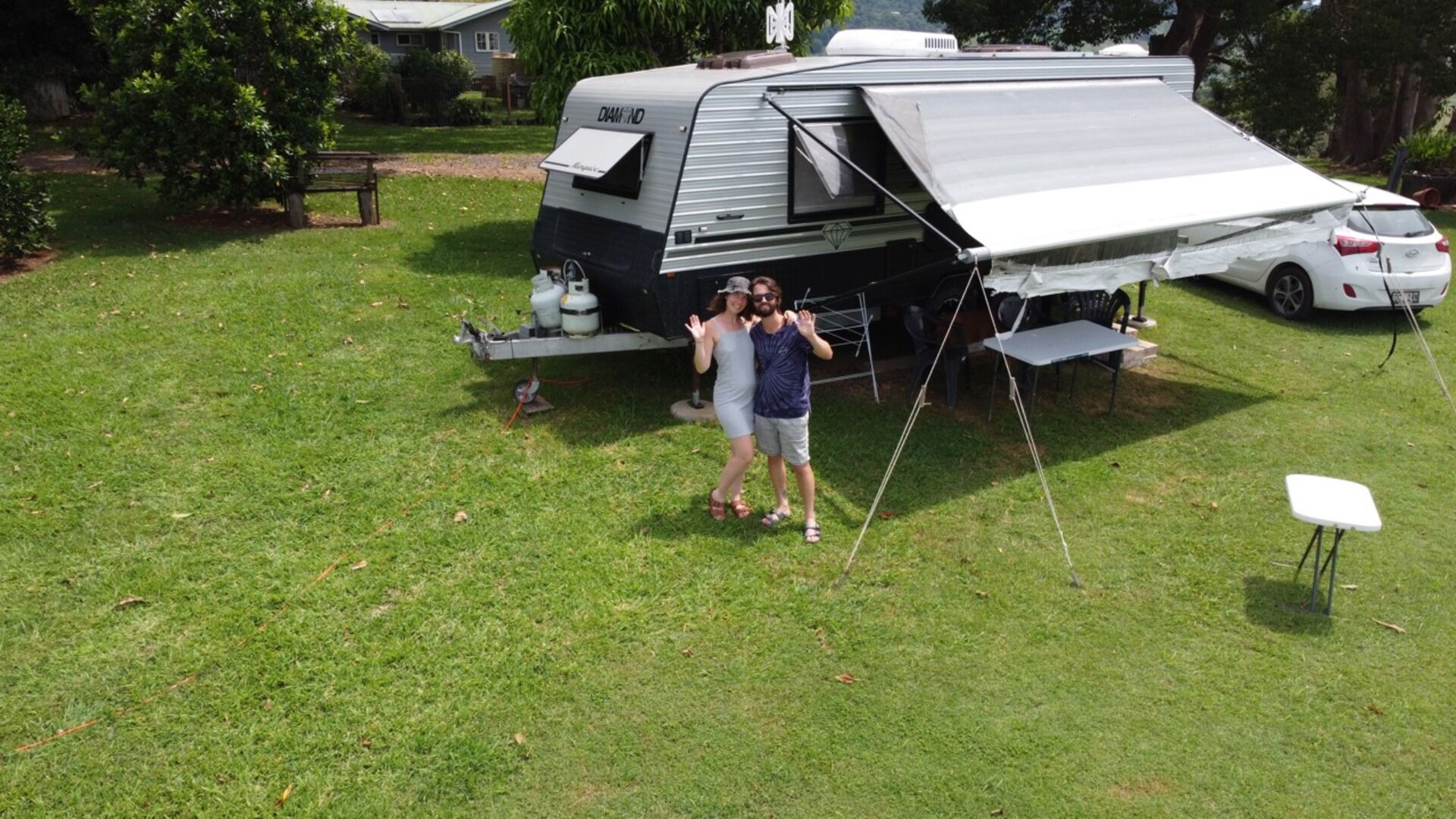 A man and woman stand beside a camper trailer, smiling and enjoying their outdoor adventure together.