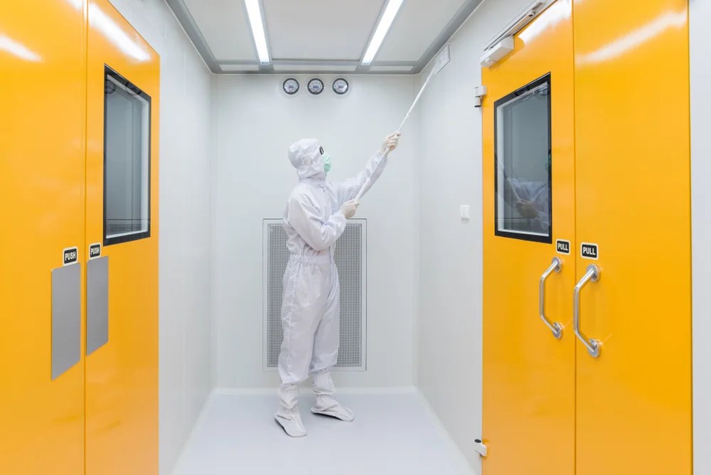 A man in a white suit is cleaning an orange door in a clean room.