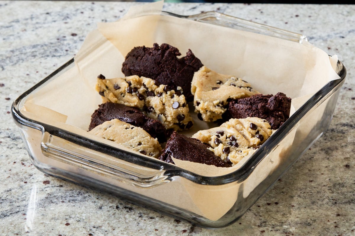 pieces of brownie batter and chocolate chip cookie dough in the lined baking pan