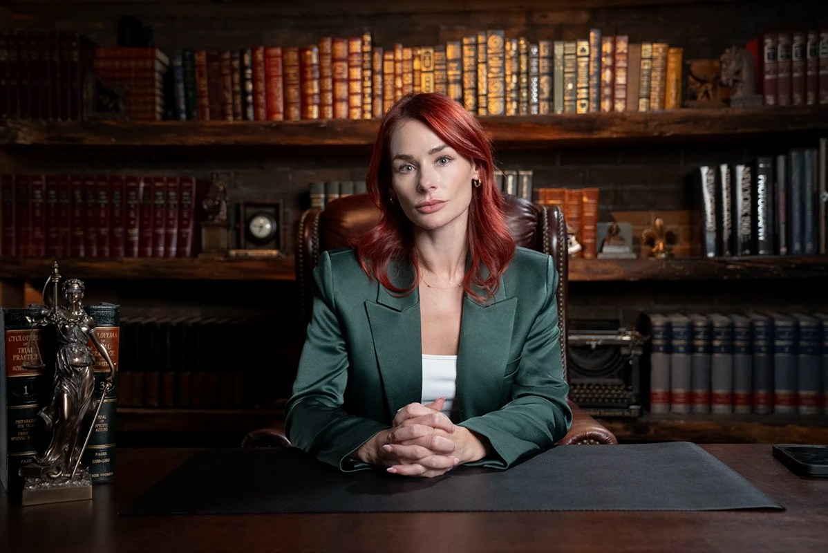 Professional business portrait of Anna Bower, senior editor at Lawfare, seated at a desk in a library setting