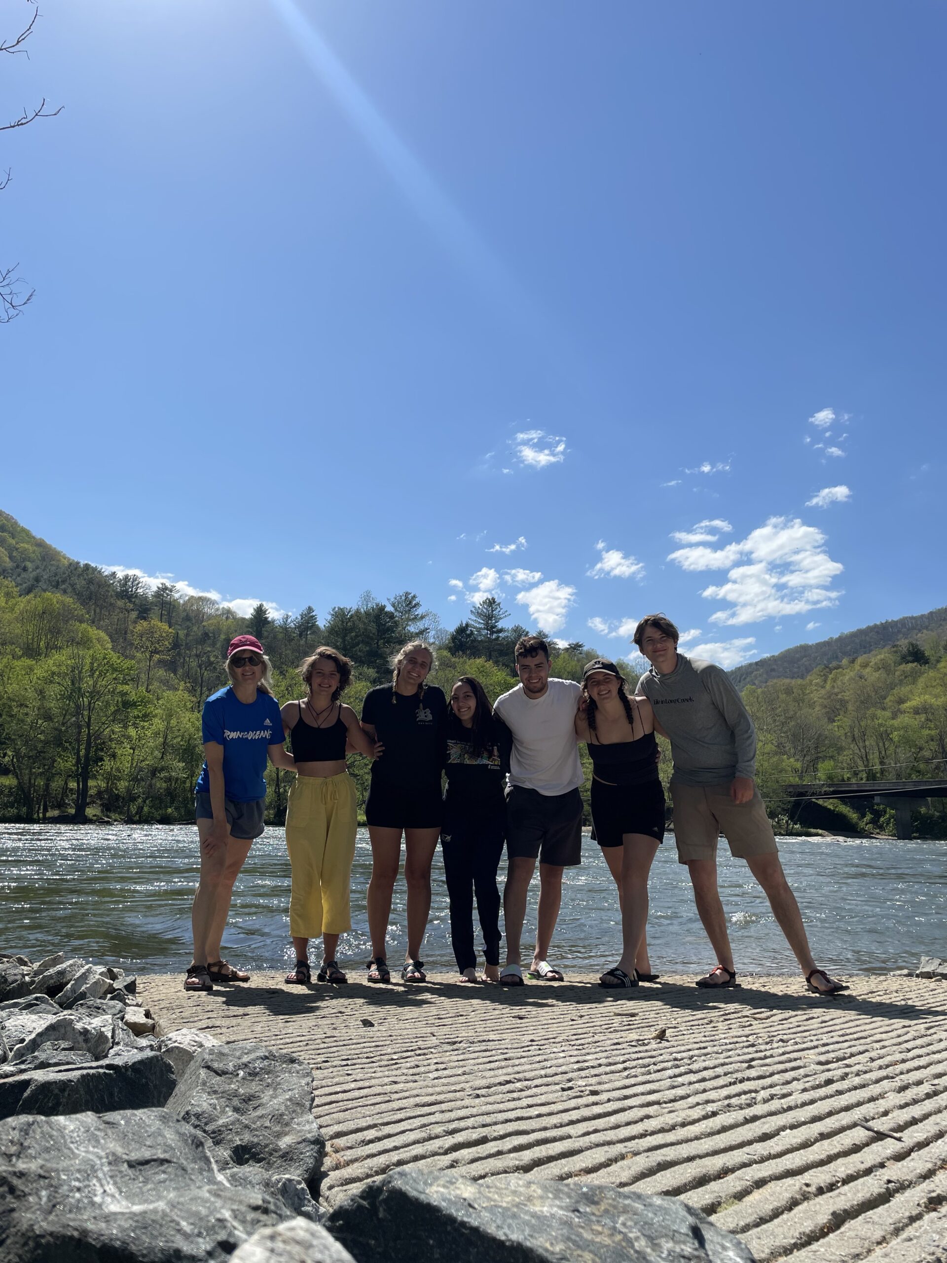 Students stand together in front of a lake on a beach.