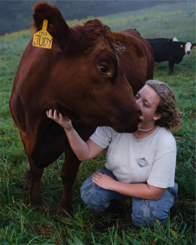 A student crouches in a pasture and holds the face of a cow close to hers.