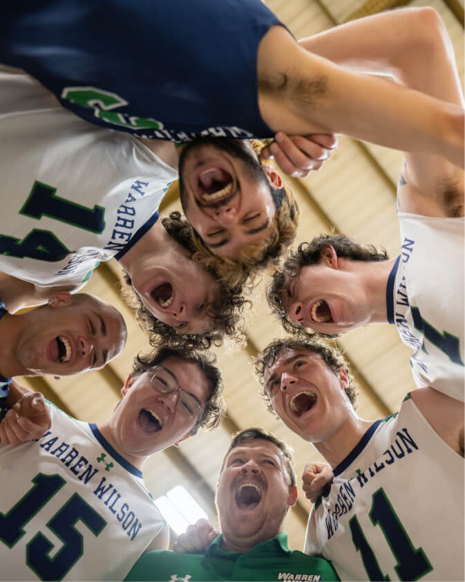 From the inside of the men's volleyball team huddle you can see the team members smiling and cheering.