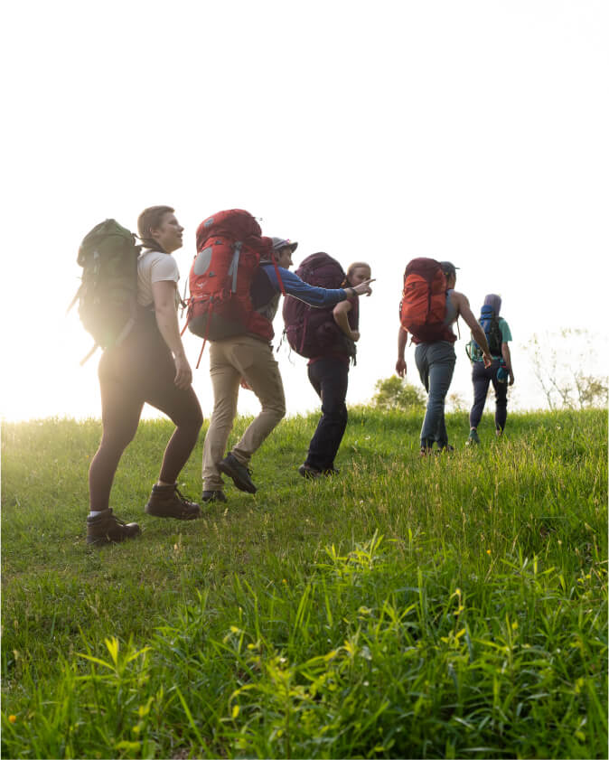A group of students hike over a grassy hill wearing backpacking gear.