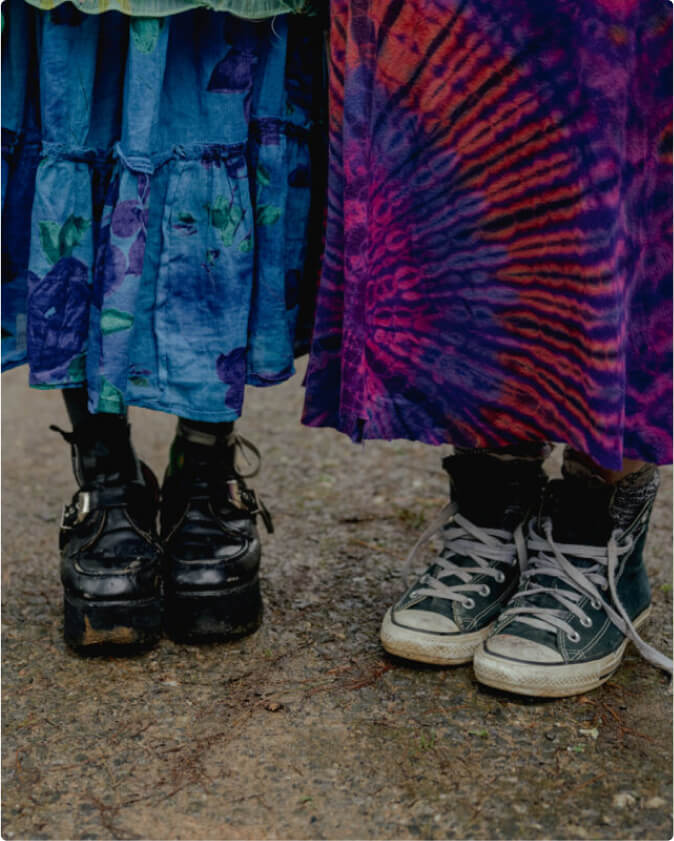 The photo is aimed at the feet of two students who are wearing colorful tie dyed skirts. One student is wearing platform shoes. The other is wearing converse.