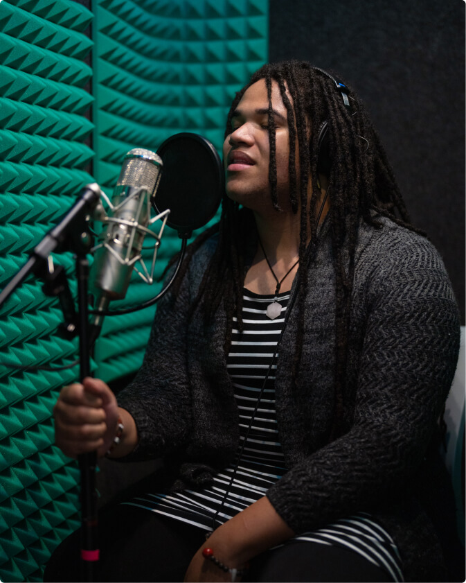 A student sits and sings in a sound booth.