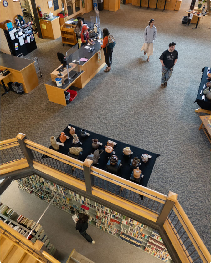 A photo taken from the loft in the library. The picture aims down capturing the circulation desk as well as the collections in the basement.